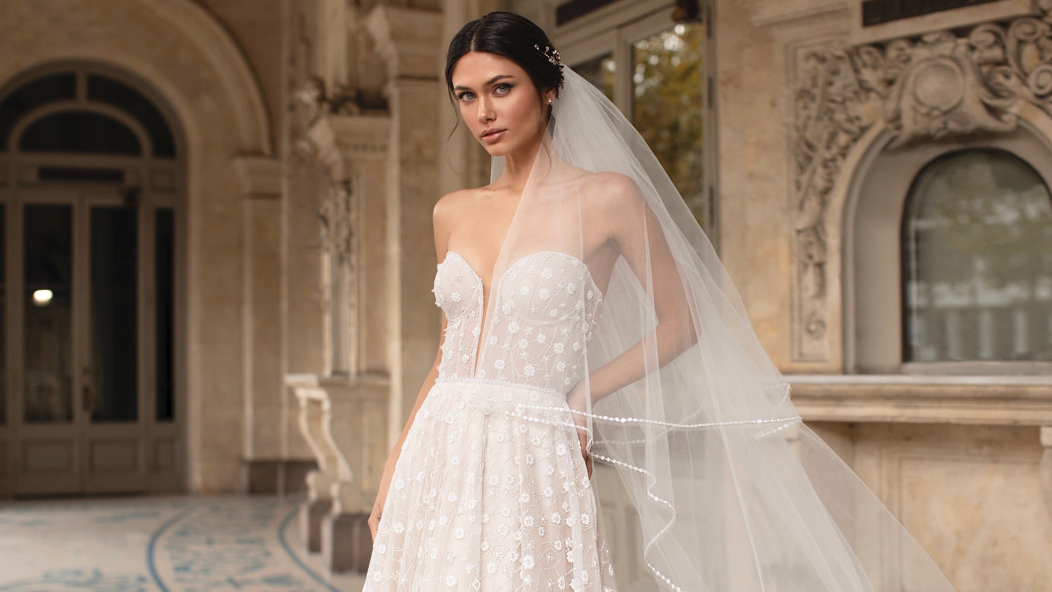 model wearing an a-line strapless wedding dress with floral and glitter detailing in a nude colour. The model also wears a 2-tier long wedding veil.